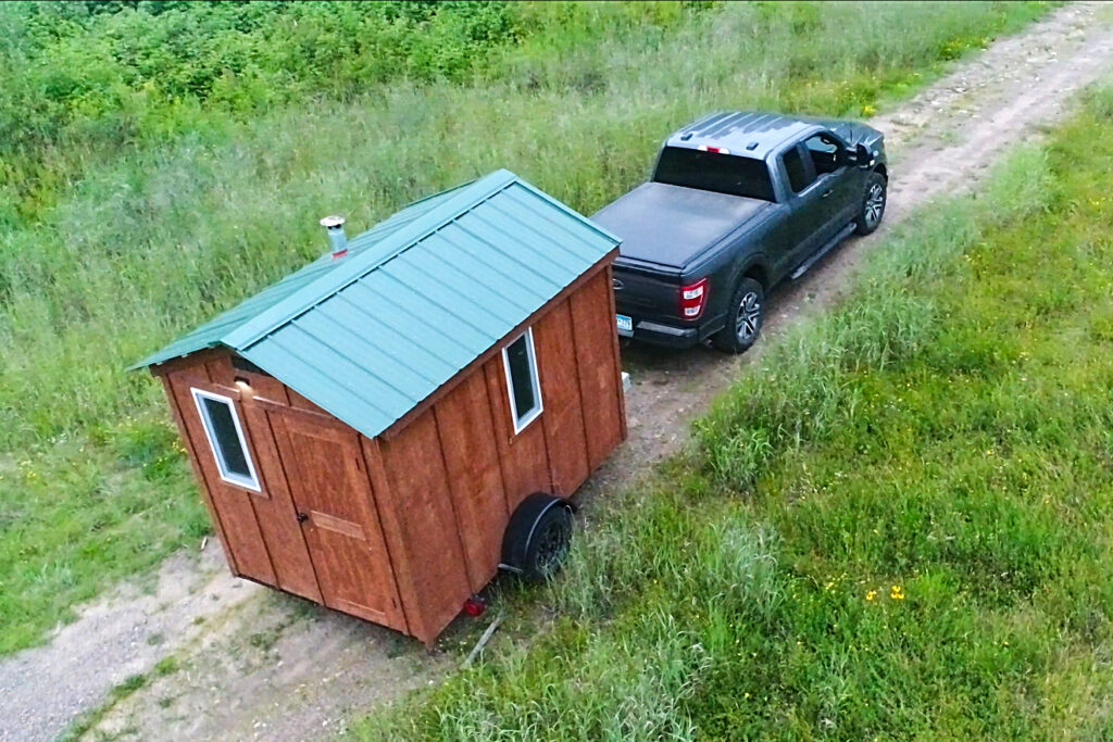 Drone aerial view of mobile sauna being towed on a dirt road through a Minnesota meadow